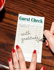 A hand writing "with gratitude" on a diner guest check