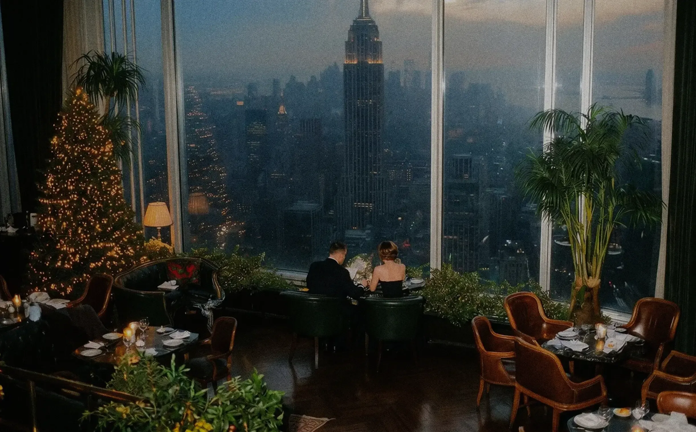 A couple dining at a high-rise restaurant overlooking the Manhattan skyline at dusk